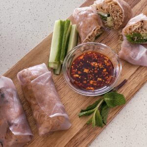 A wooden cutting board featuring a bowl of sauce alongside freshly baked rolls.