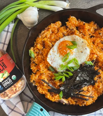 Kimchi fried rice topped with a sunny-side-up egg, sliced green onions, and seaweed strips in a black cast-iron skillet next to a jar of Ocean's Halo kimchi and a box of sticky rice.