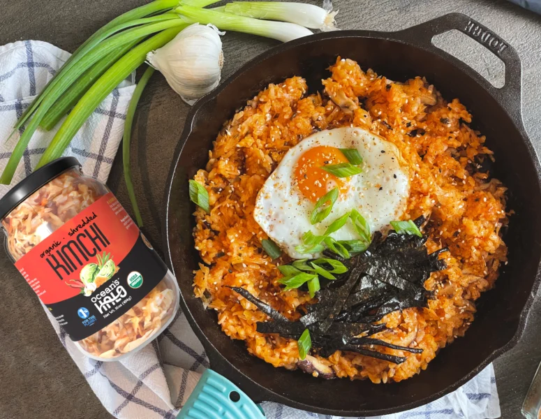 Kimchi fried rice topped with a sunny-side-up egg, sliced green onions, and seaweed strips in a black cast-iron skillet next to a jar of Ocean's Halo kimchi and a box of sticky rice.