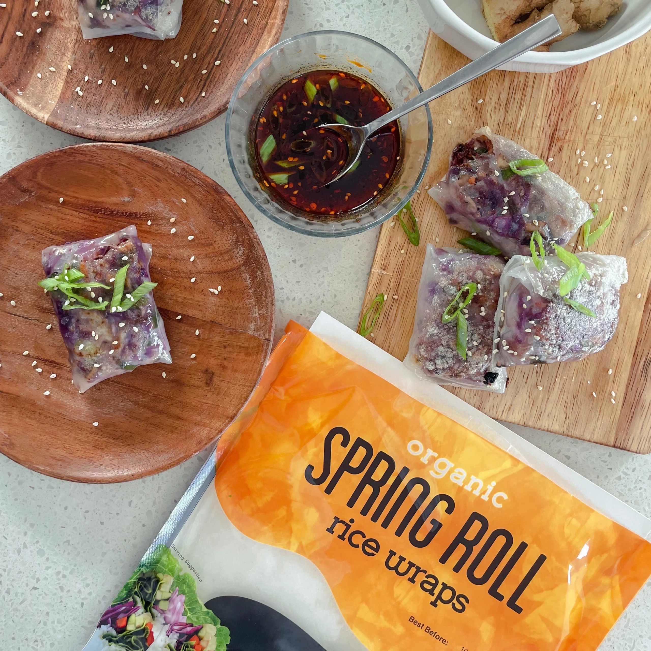 Spring rolls stuffed with purple cabbage and noodles served with dipping sauce next to Ocean's Halo Rice Wraps.
