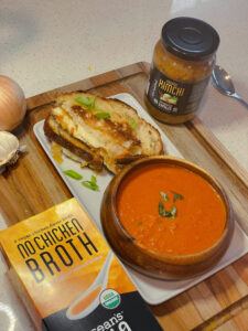 A plate with Tomato Soup and Kimchi Grilled cheese on it with Ocean’s Halo No Chicken Broth and Kimchi next to it.