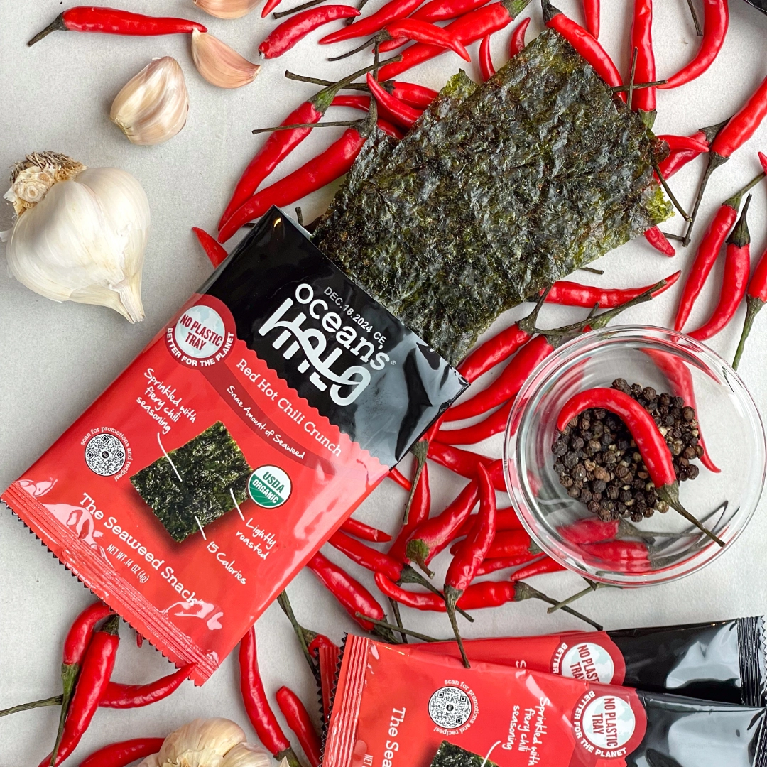 Ocean's Halo Red Hot Chili Crunch seaweed snack package surrounded by whole red chili peppers and garlic cloves.