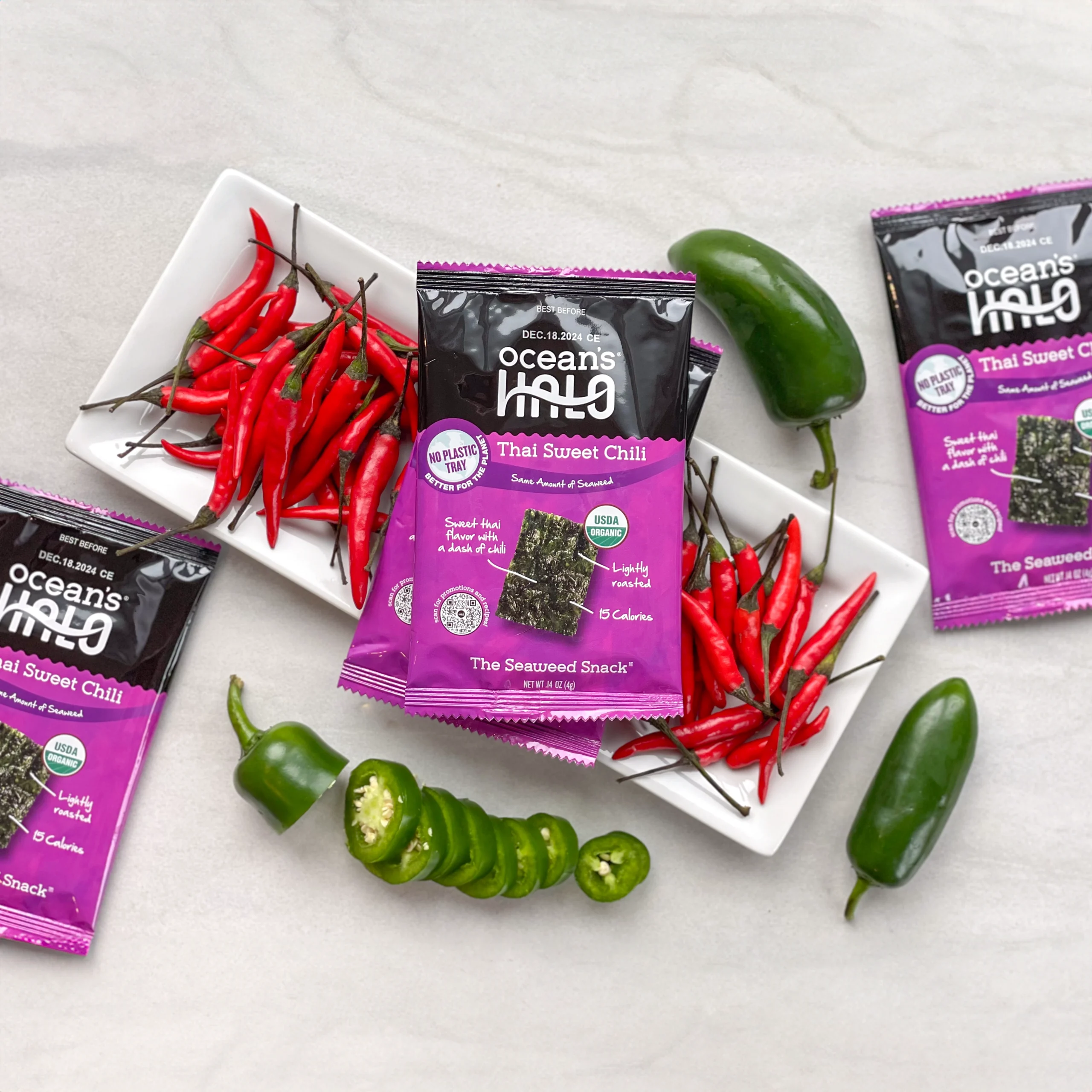 Ocean's Halo Thai Sweet Chili seaweed snack packages arranged with fresh red chilis and sliced jalape?os.