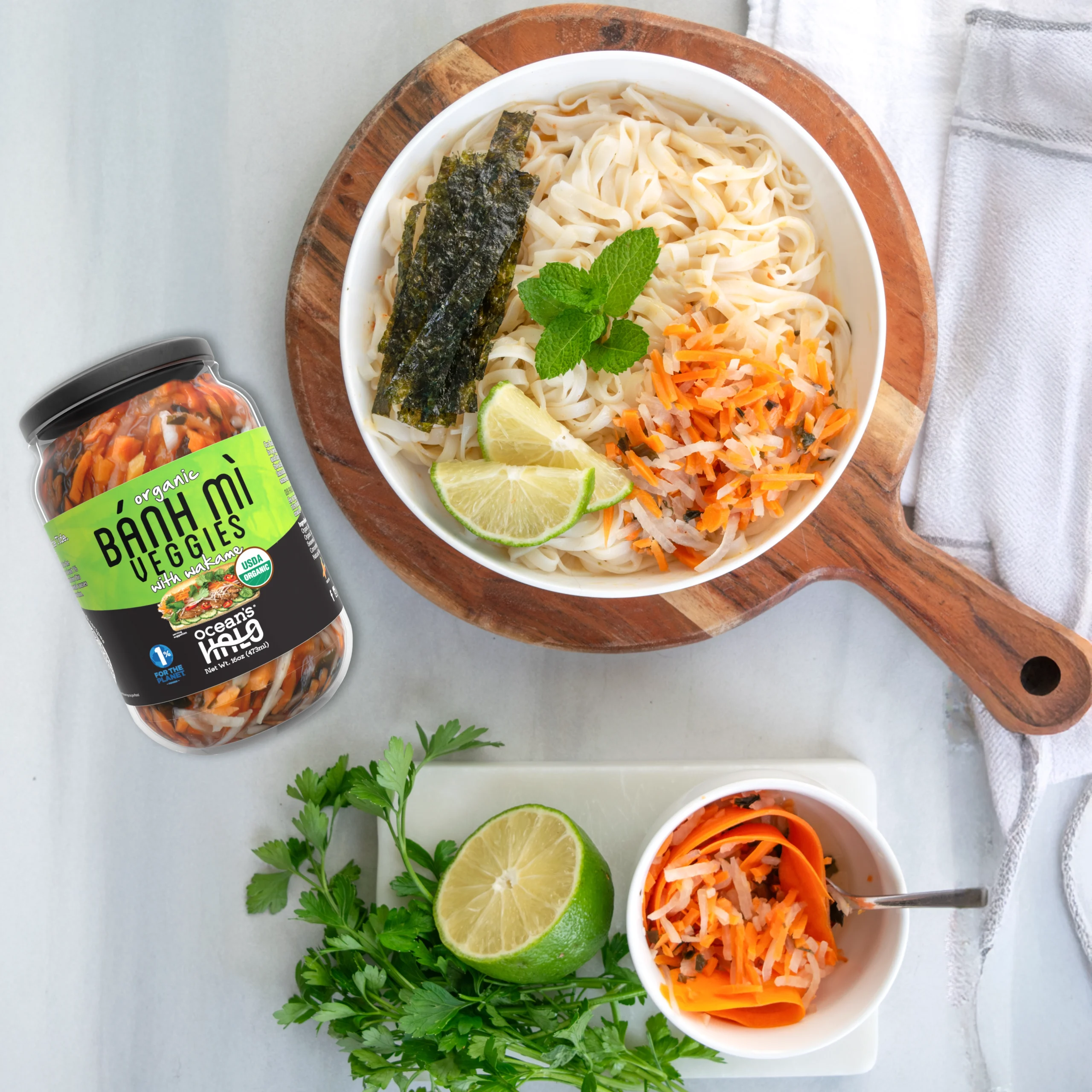 A noodle bowl topped with lime, mint, and pickled carrots next to a jar of Ocean's Halo B?nh M? Veggies.