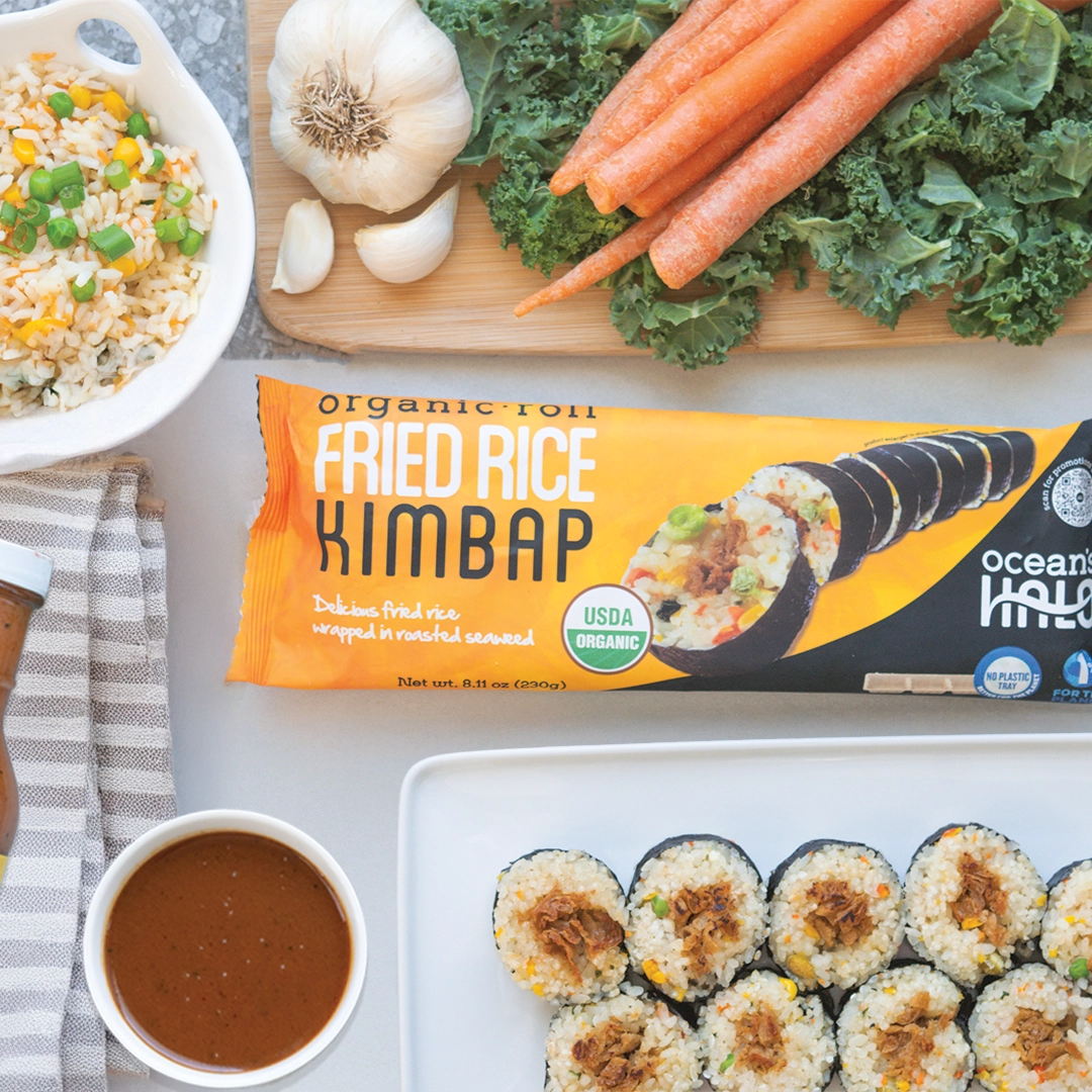 Ocean's Halo Fried Rice Roll Kimbap package alongside sliced kimbap pieces, a bowl of dipping sauce, and raw vegetables.