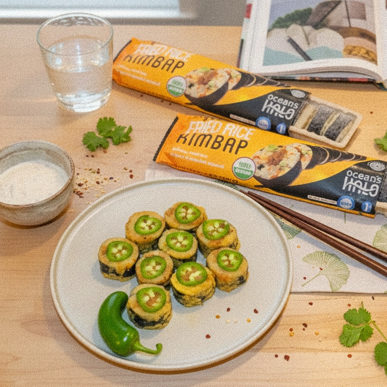 Plate of fried rice roll slices topped with jalape?o rounds, served next to Ocean's Halo packaging, dipping sauce, and water.