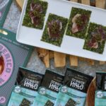 A white platter holds four seaweed snacks topped with iberico ham and caviar, surrounded by Ocean's Halo snack packs.