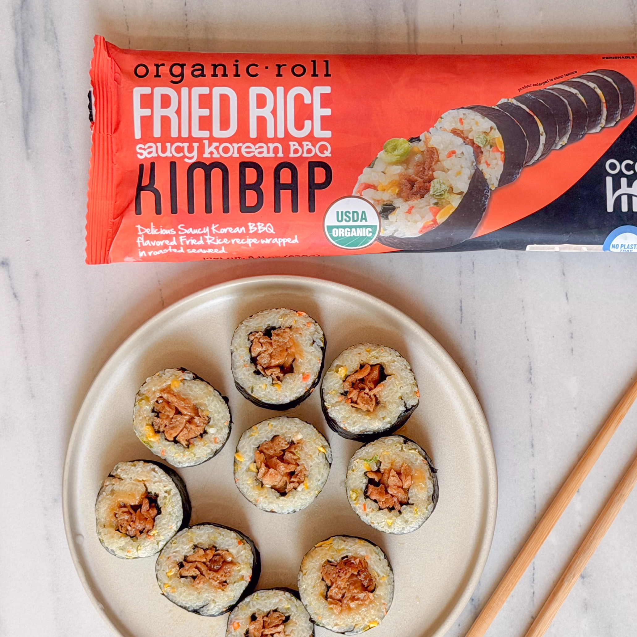 Top-down view of sliced fried rice roll on a beige plate next to chopsticks and Ocean's Halo Saucy Korean BBQ Fried Rice Roll packaging.