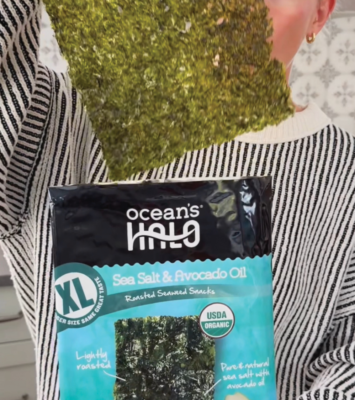 a woman pulling out an extra large seaweed snack from a package labeled as organic XL seaweed snacks. Sea Salt & avocado oil flavor.