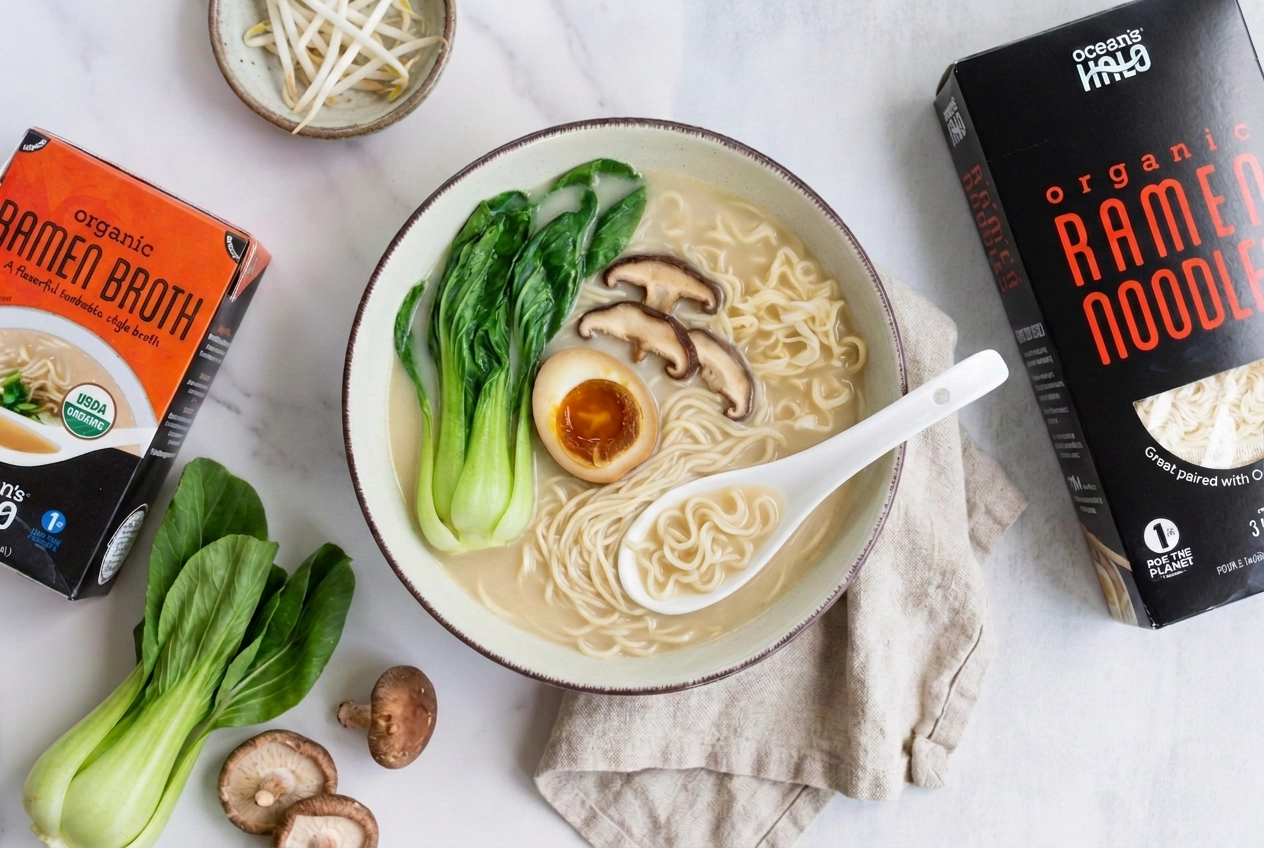 Bowl of ramen topped with egg, bok choy, and mushrooms next to Ocean's Halo broth and noodle packages.
